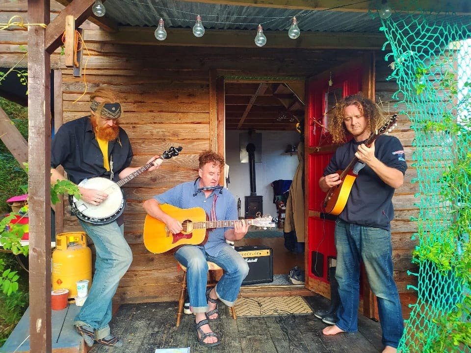 Rud Sin performing together outside a wooden studio.